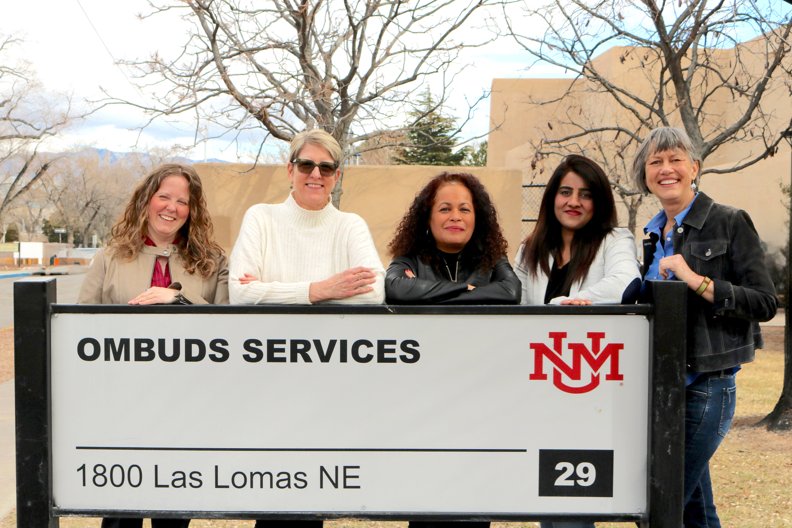 Ombuds Services team standing behind the Ombuds Services building sign